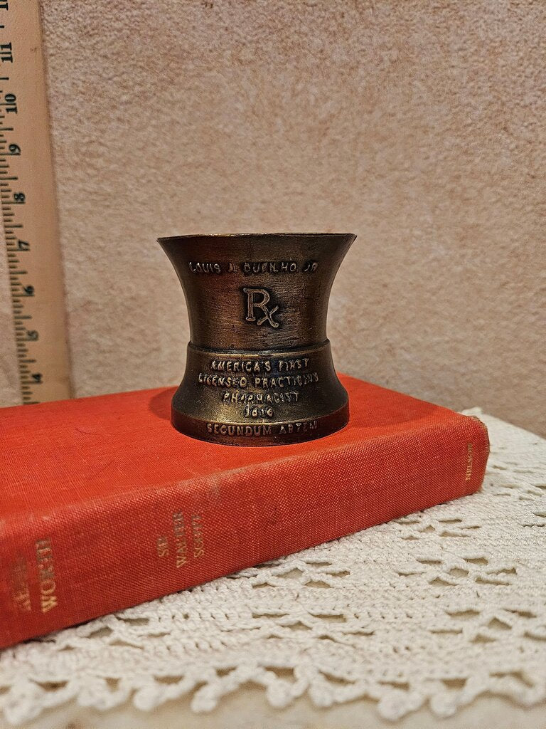 A vintage bronze pharmacy mortar and pestle, a symbol of the pharmacy profession, featuring intricate designs and historical inscriptions.